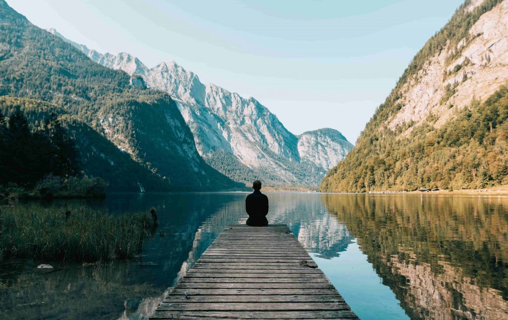 persona meditando frente a un lago y una montaña